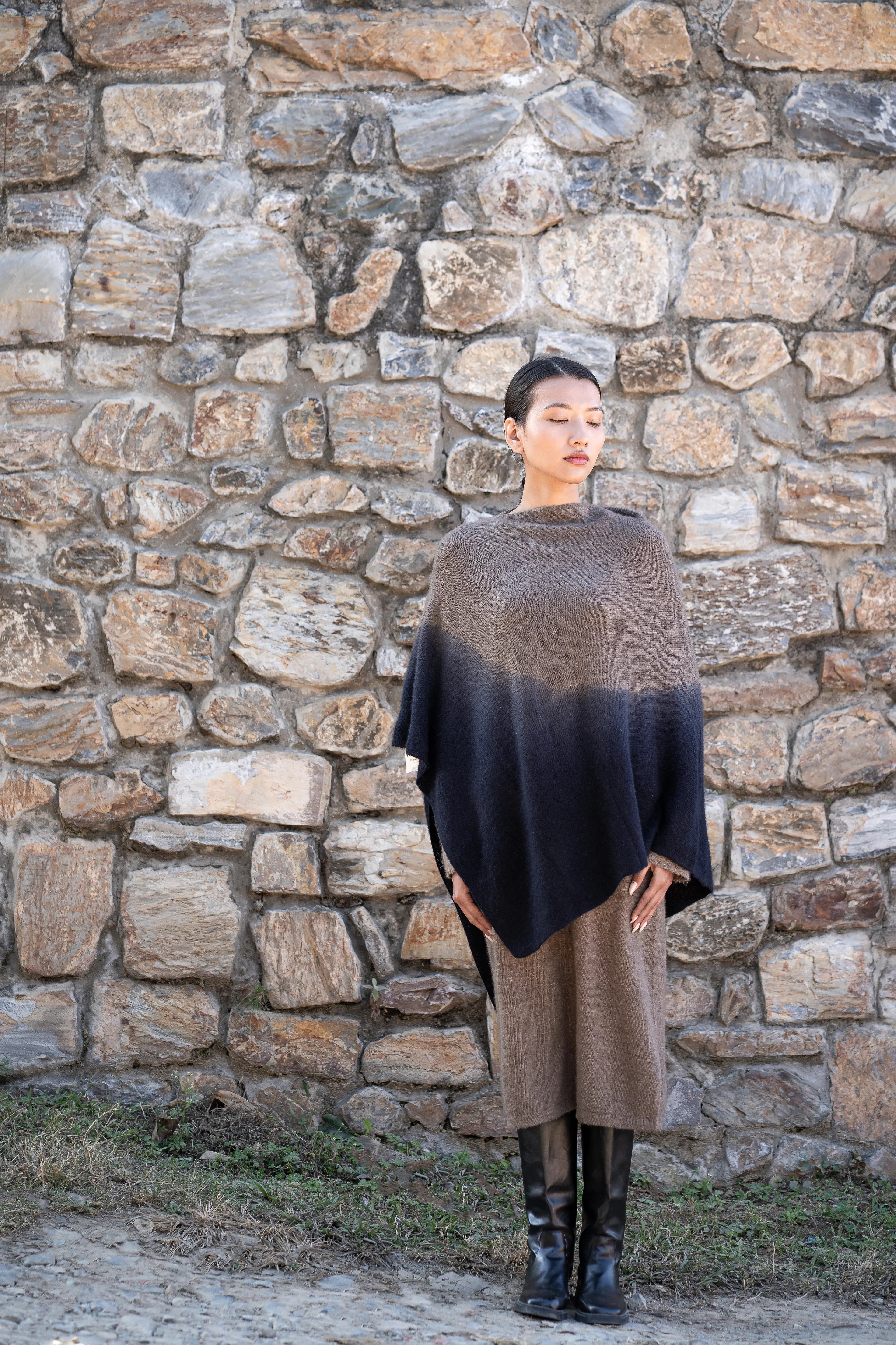 Model in a taupe and charcoal dip-dyed cashmere poncho against a stone wall