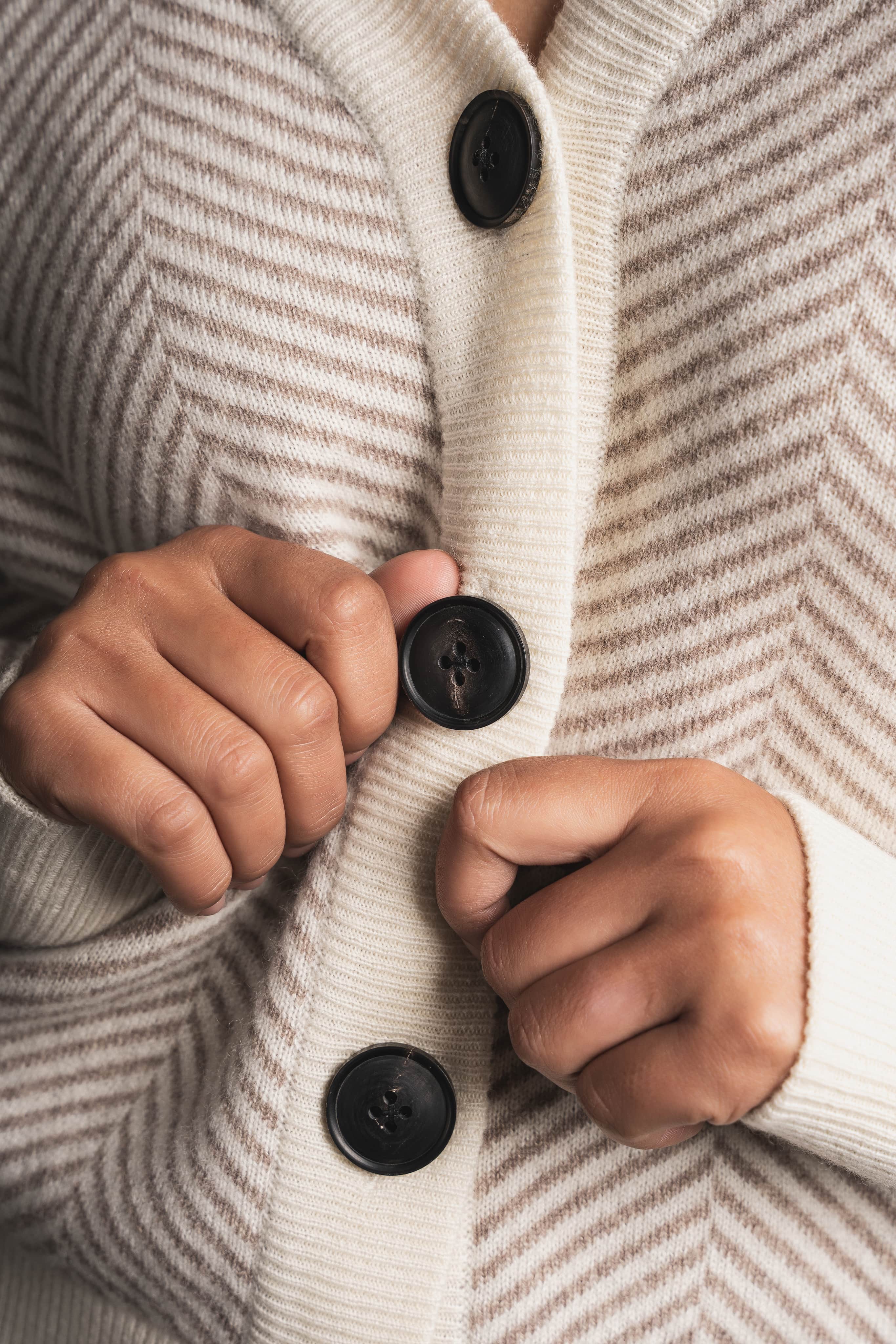 Hands buttoning a herringbone cashmere cardigan
