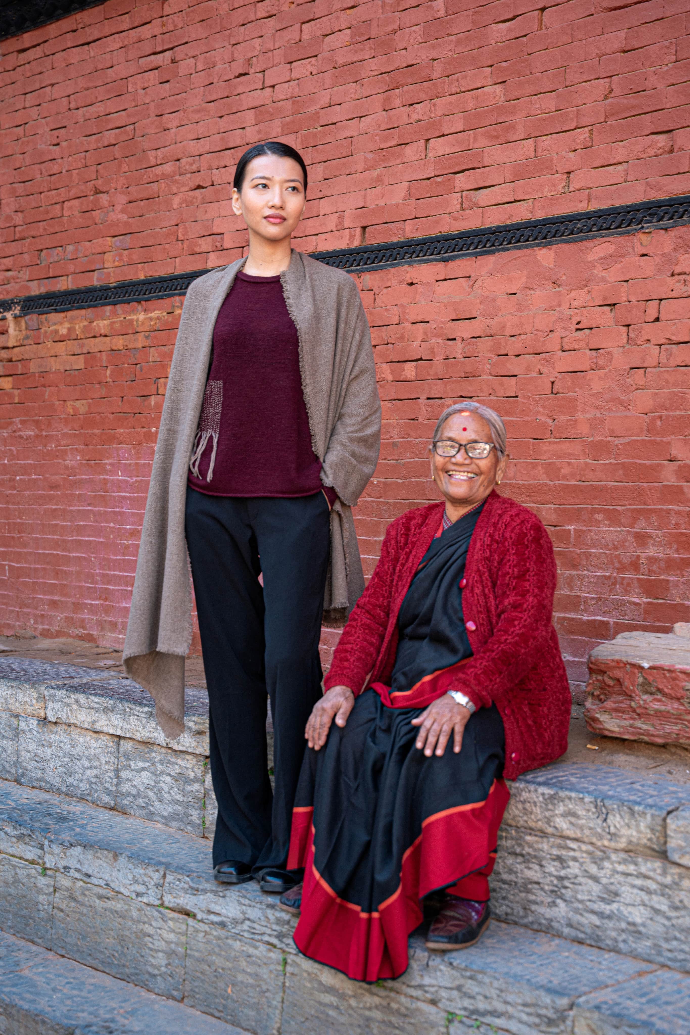 Two women wearing KPA cashmere pieces in front of a brick wall
