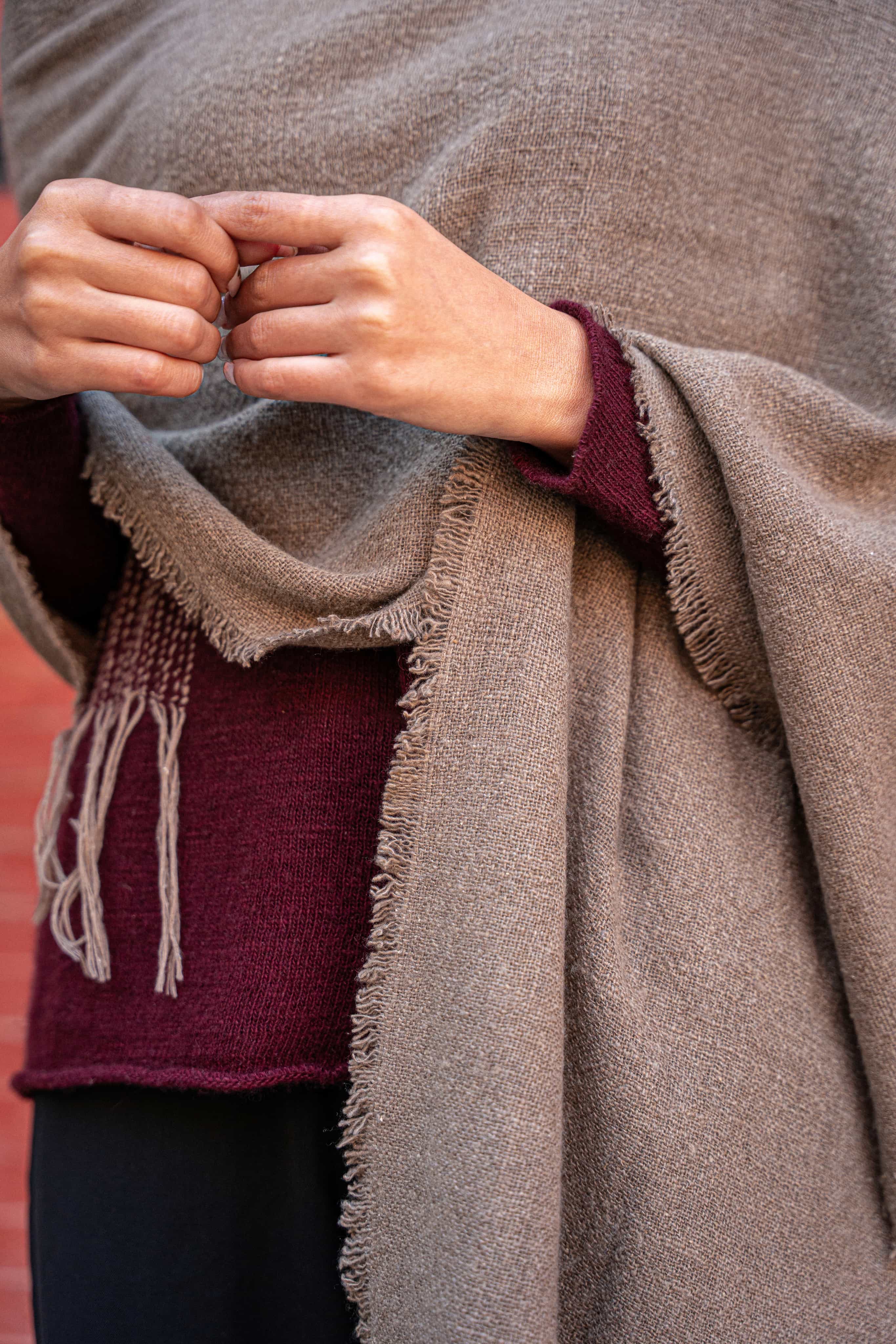 Model draping a fringe-trimmed raw cashmere wrap over maroon knitwear